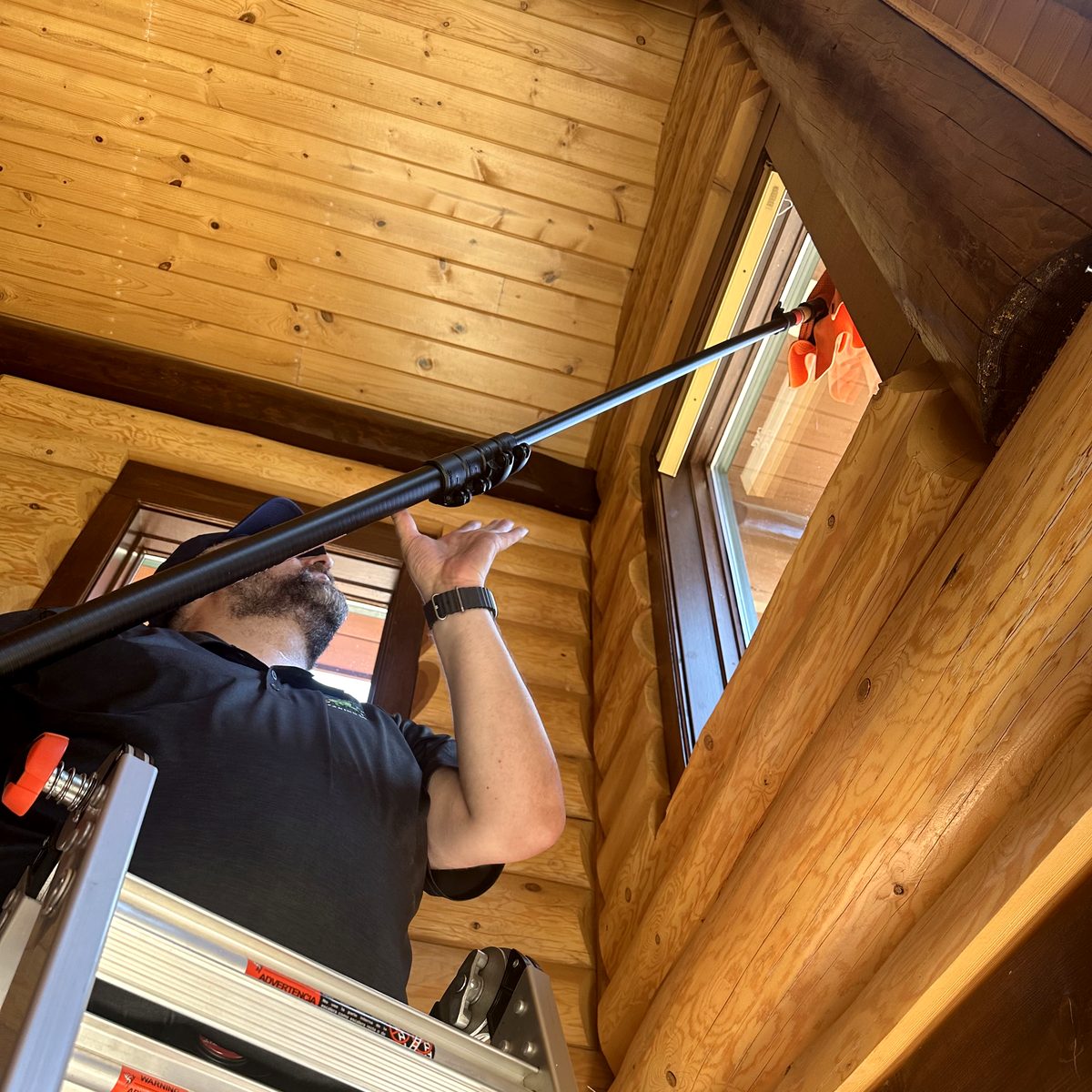 Technician cleaning a high window in a log cabin from a ladder