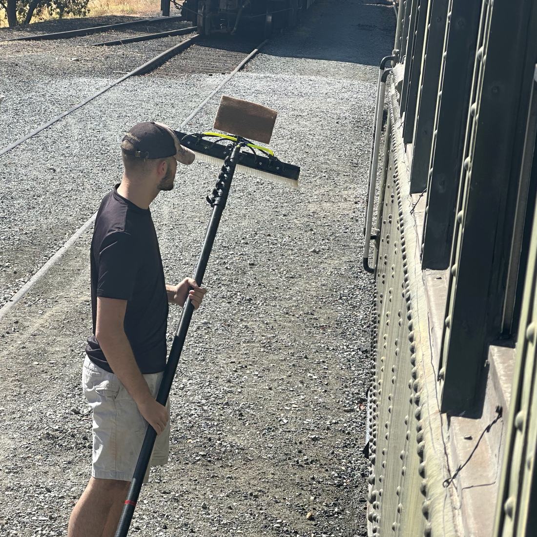 Crew member washing a historic railcar with a water-fed pole